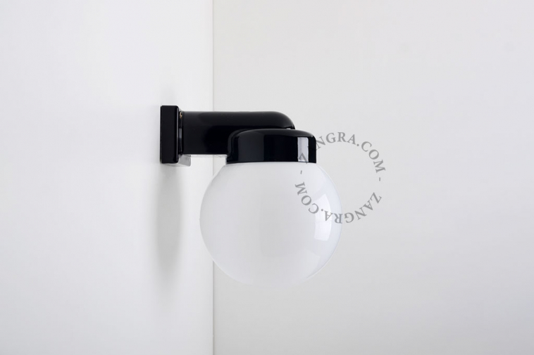 Black porcelain wall light with glass globe for bathroom or outdoor use.