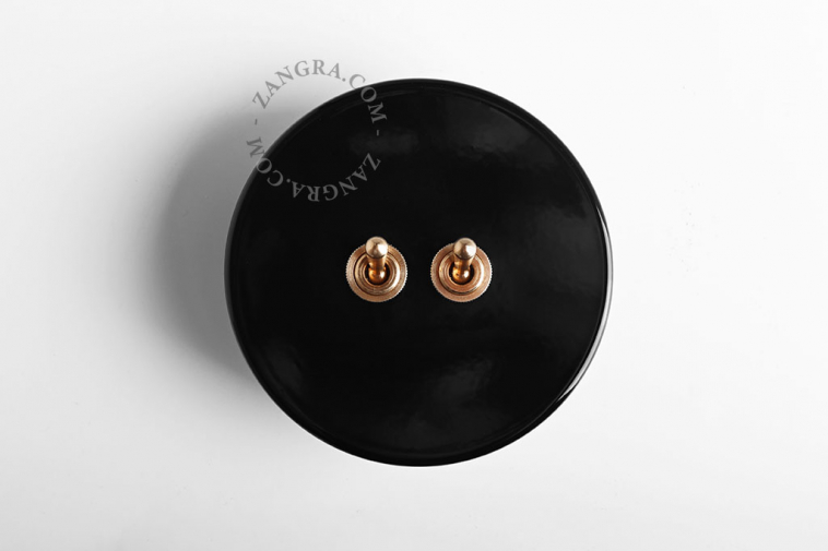 Round black light switch with 2 brass levers.