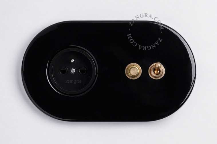 Black flush mount outlet & switch with raw brass toggle & pushbutton.