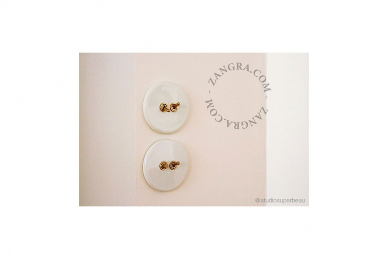 White porcelain switch with double toggle in brass.