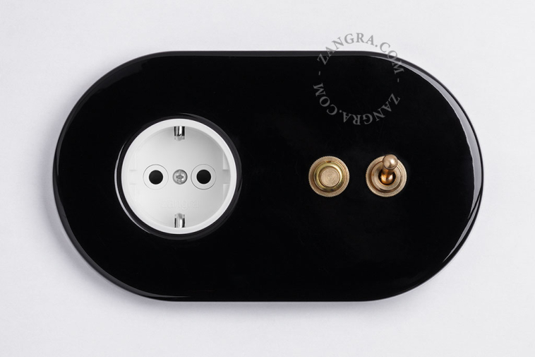 Black flush mount outlet & switch with raw brass toggle & pushbutton.