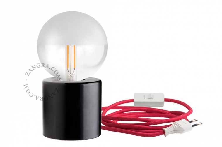 Black porcelain table lamp with exposed light bulb and red cable.