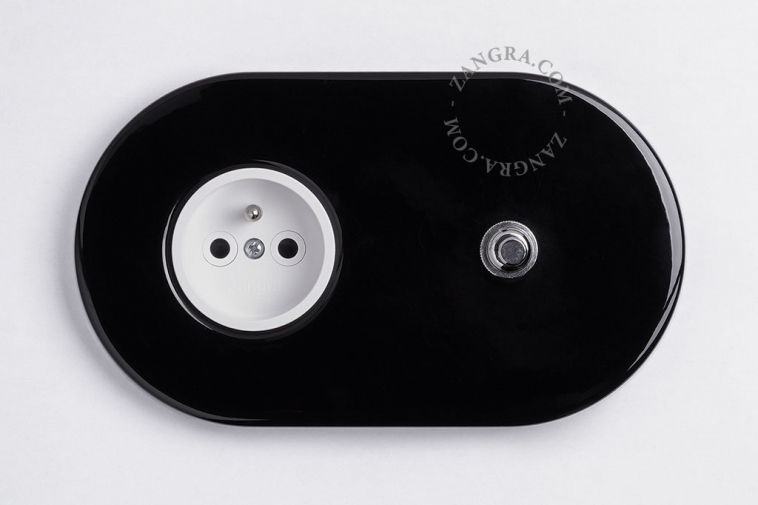 Interrupteur à bouton-poussoir en laiton nickele avec une prise murale noire.