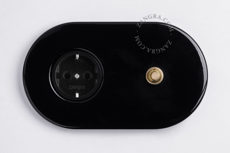 Black flush mount outlet & switch with raw brass pushbutton.