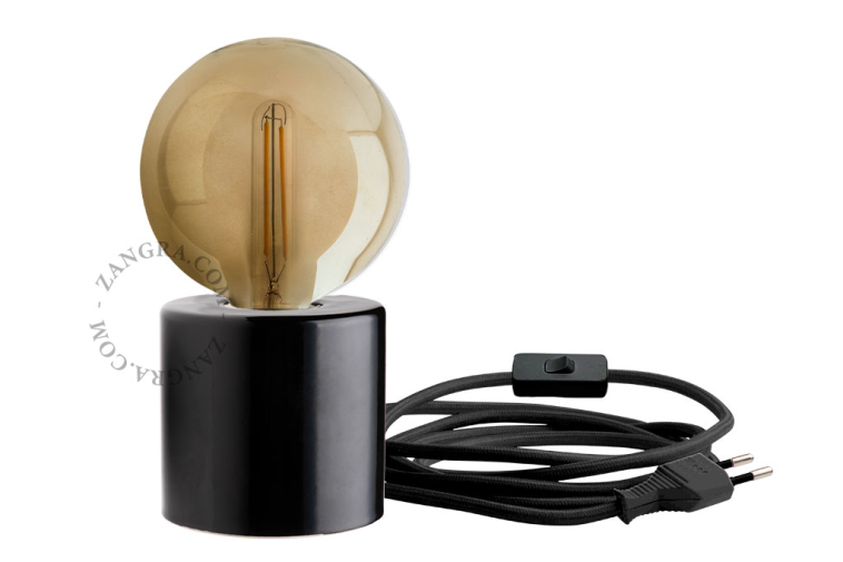 Bedside table lamp in black porcelain with exposed light bulb.