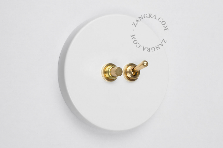 Round white two-way light switch with brass toggle and pushbutton