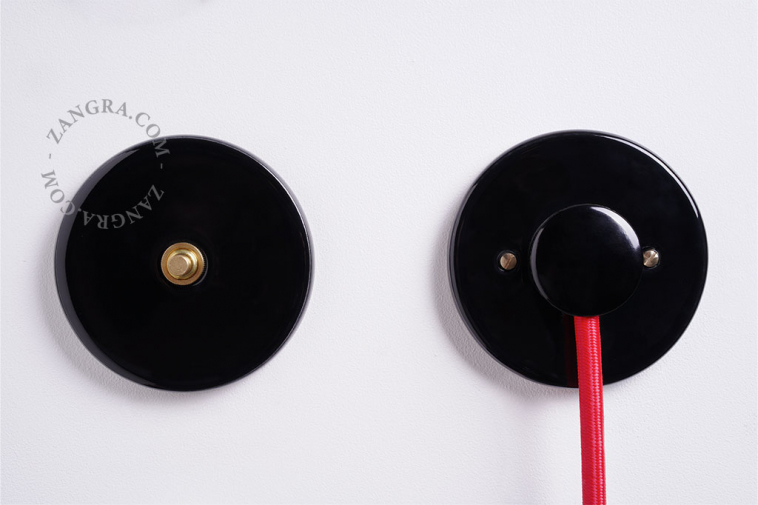Interrupteur en porcelaine noire avec bouton-poussoir en laiton brut.