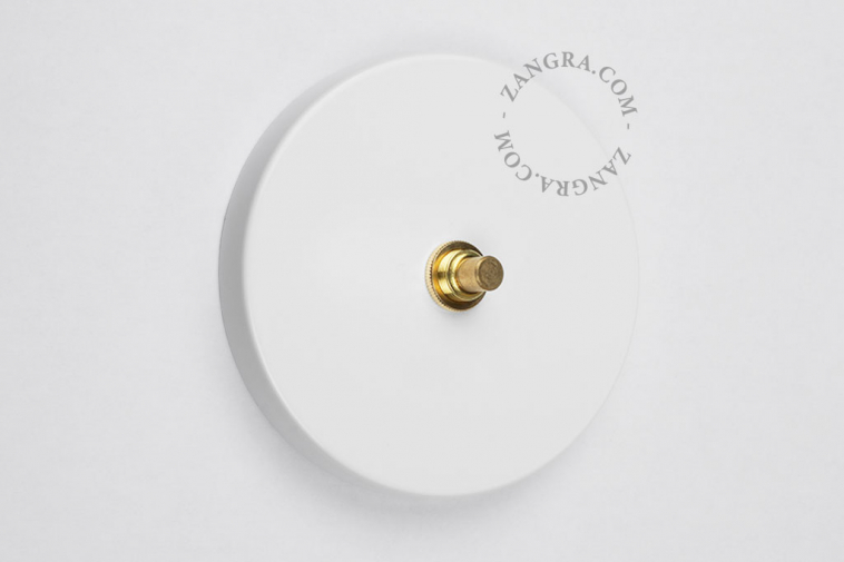 Interrupteur blanc rond avec bouton-poussoir en laiton brut.