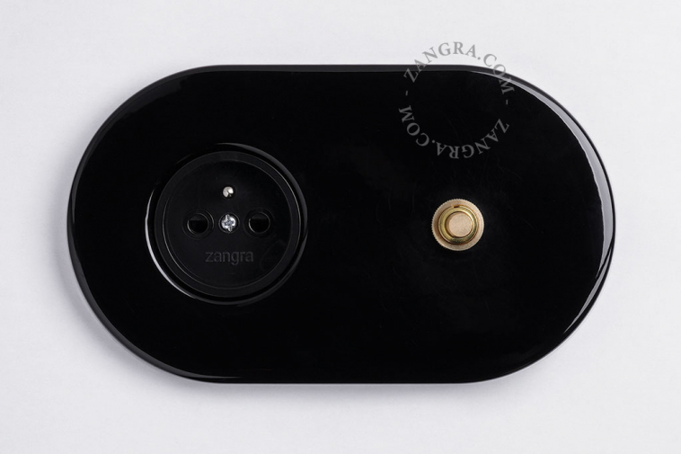 Black flush mount outlet & switch with raw brass pushbutton.