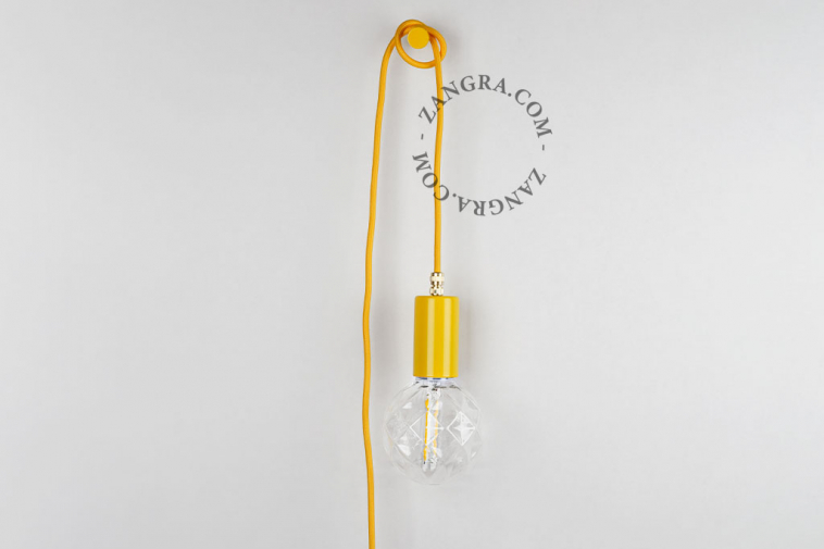 Gele looplamp met textielsnoer, lichtknipper en stekker om op te hangen aan de wand.