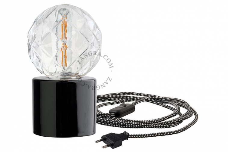 Black porcelain table lamp with exposed light bulb.